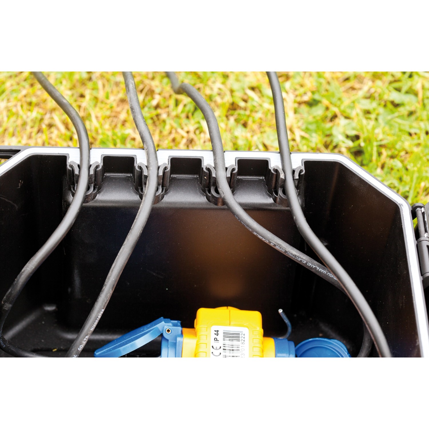 Heissner Garden Power Box: Schwarze Stromverteilerbox mit Kabeln und Stecker im Garten.