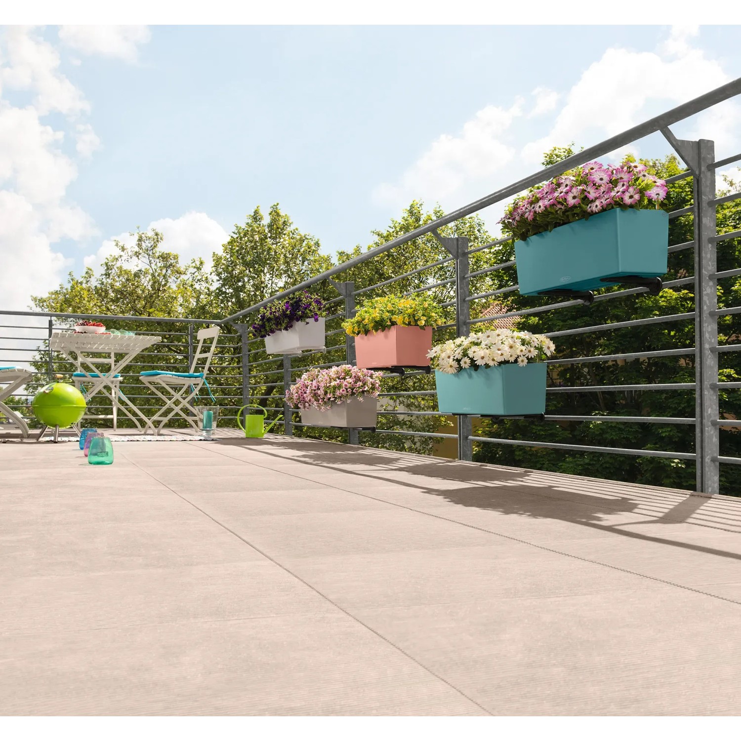 Mehrere bepflanzte Lechuza Balconera Blumenkästen in verschiedenen Farben am Balkongeländer.