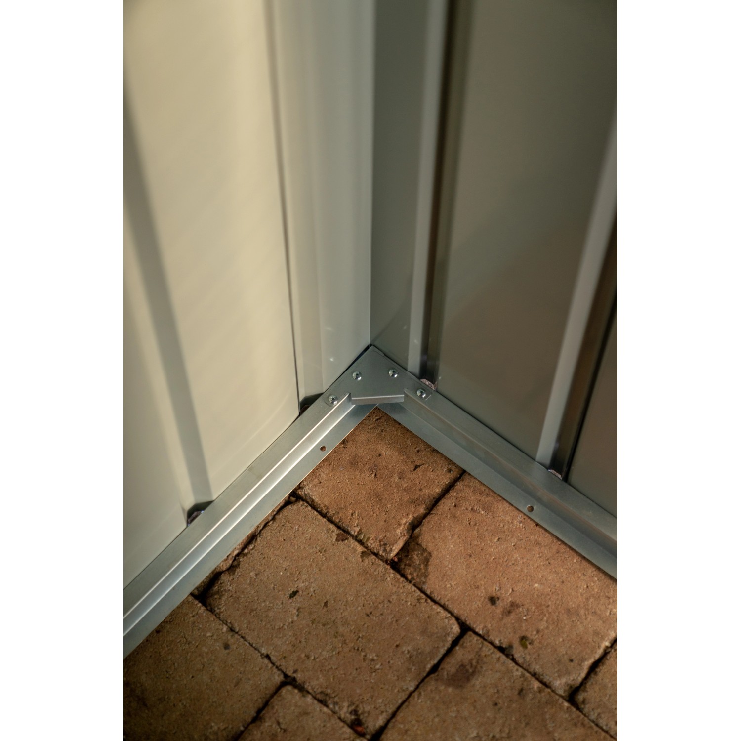 Detailaufnahme: Ecke des Globel Metall-Anlehngerätehauses Lean-To in Anthrazit mit Bodenbefestigung.