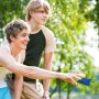 Zwei junge Männer spielen Cornhole Wurfspiel im Freien. Einer wirft ein blaues Bean Bag Säckchen, ideal für Freizeit & Garten.