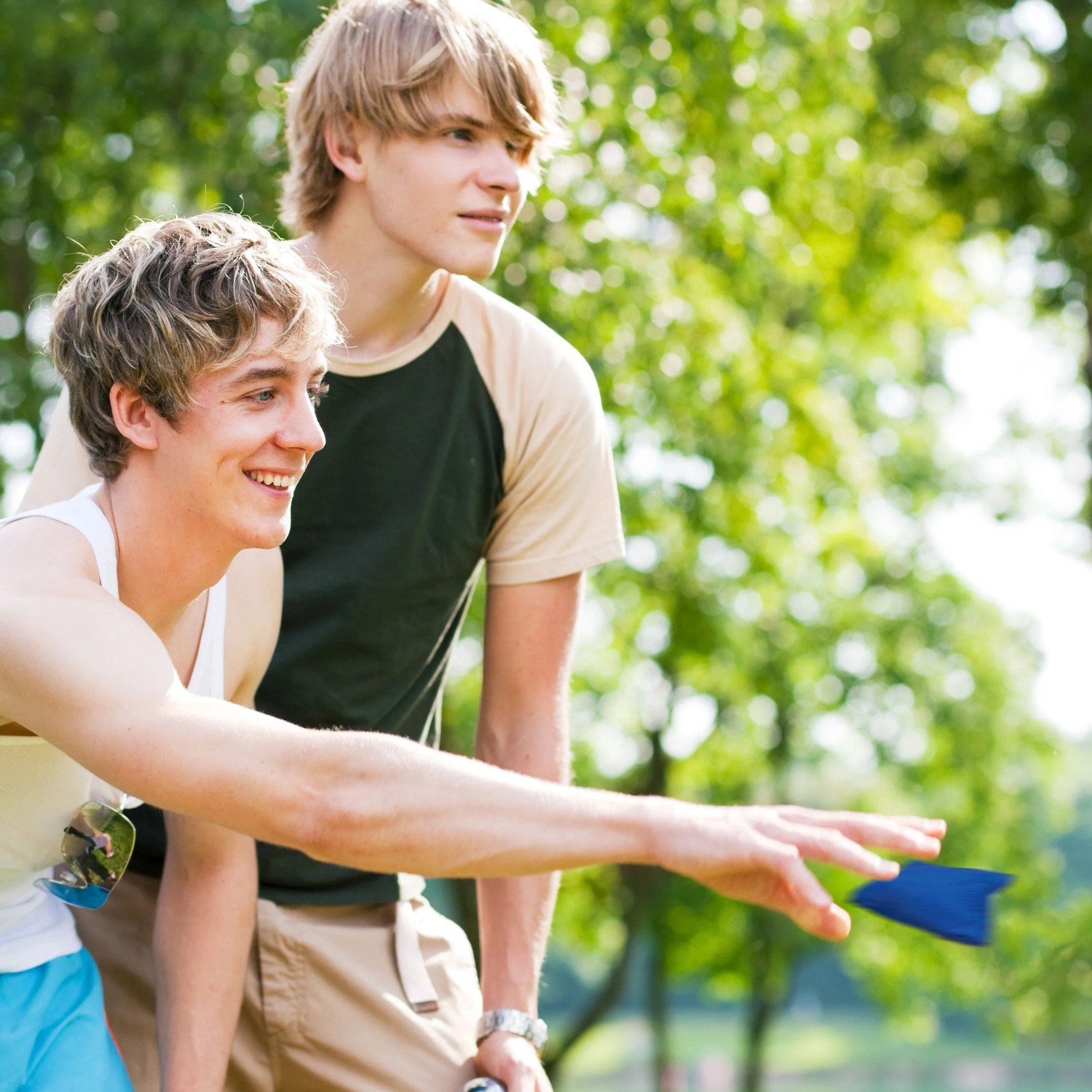 Zwei junge Männer spielen Cornhole Wurfspiel im Freien. Einer wirft ein blaues Bean Bag Säckchen, ideal für Freizeit & Garten.