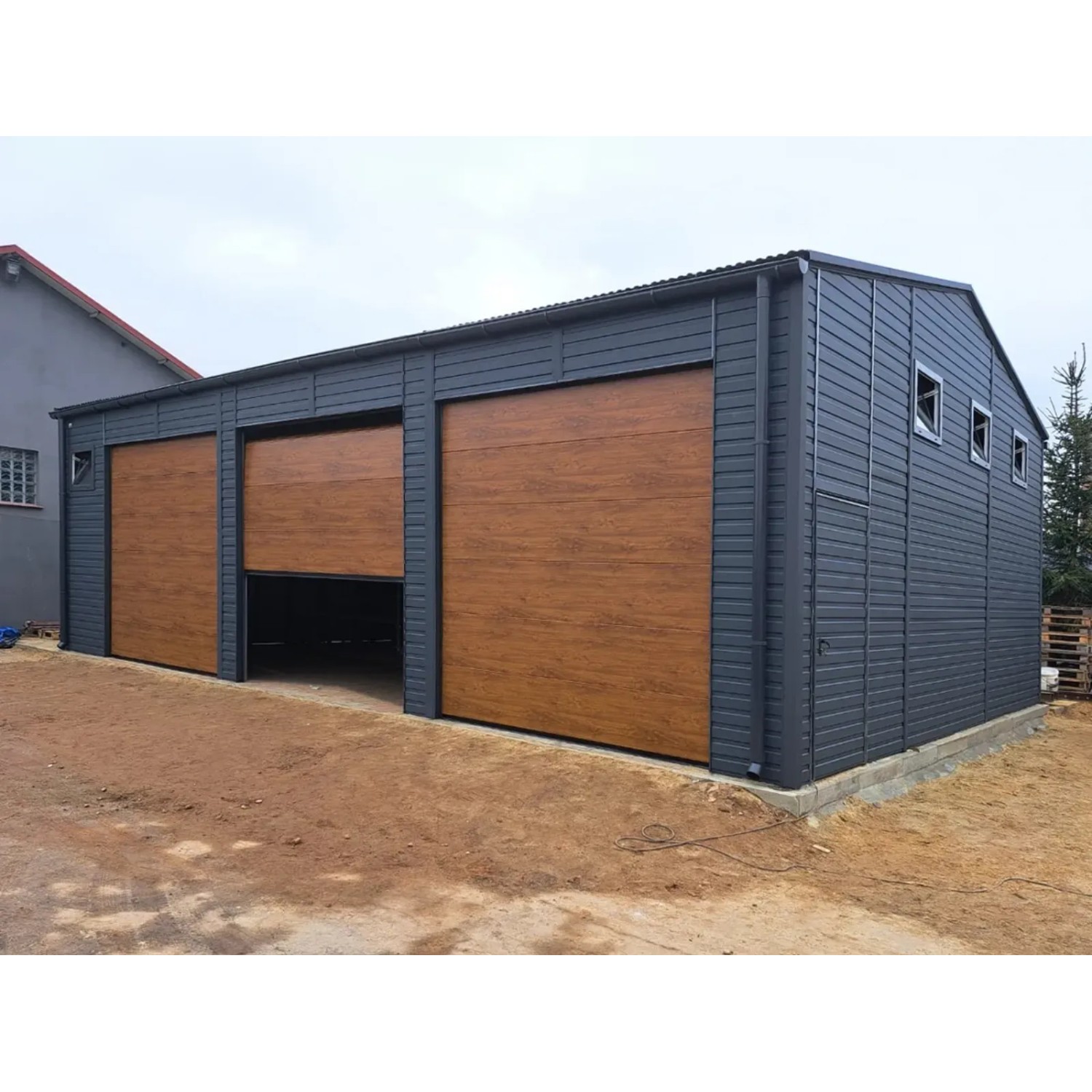 Große Liderstal Fertiggarage aus Graphit-Blech mit drei Sektionaltoren in Goldene Eiche, eines offen, und Fenstern.