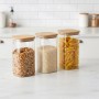 3er Set eckige Vorratsgläser aus Glas mit luftdichten Bambusdeckeln, gefüllt mit Müsli, Reis und Nudeln, auf Küchentheke.