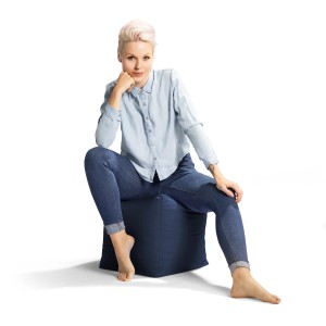 Frau sitzt auf blauem Sitting Point Hocker Cube Scuba 60 l im Jeanslook.