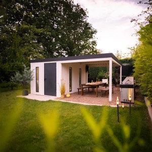 Modernes, weißes Gartenhaus Amazing Spaces Urban One mit Überdachung und Esstisch im Garten.