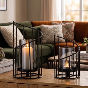 Zwei schwarze Eisen-Windlichter mit transparenten Glaszylindern und brennenden Kerzen auf einem Holztisch. 2er Set Kerzenhalter.