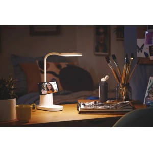 Weiße Philips LED Schreibtischleuchte Bucket mit Handy im Stifthalter auf einem Schreibtisch.