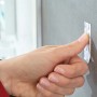 Anbringen eines Tesa Powerstrips Waterproof Klebestreifens an einer grauen Fliese im Badezimmer.