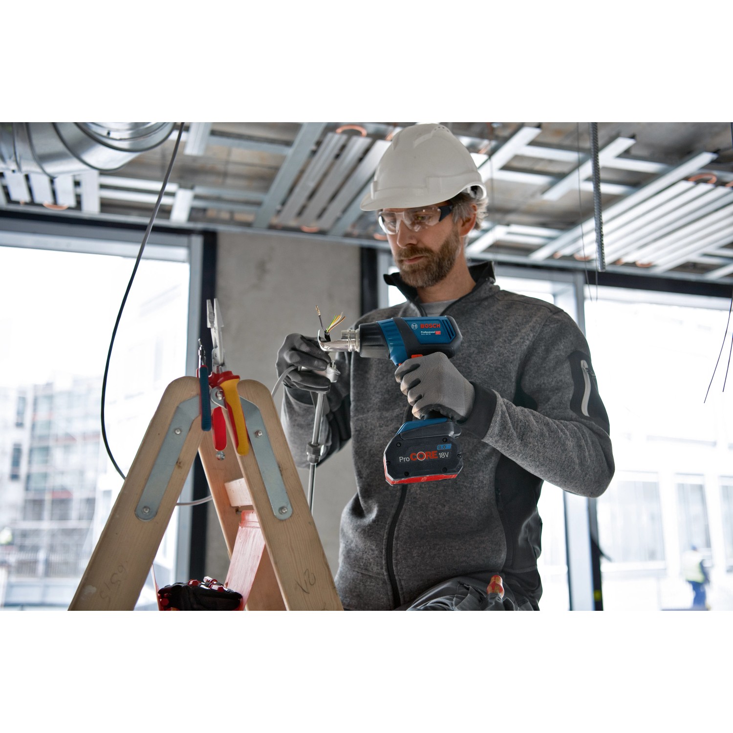 Bosch Professional Akku-Heißluftgebläse GHG 18V-50 in Anwendung, mit Arbeiter auf Leiter.