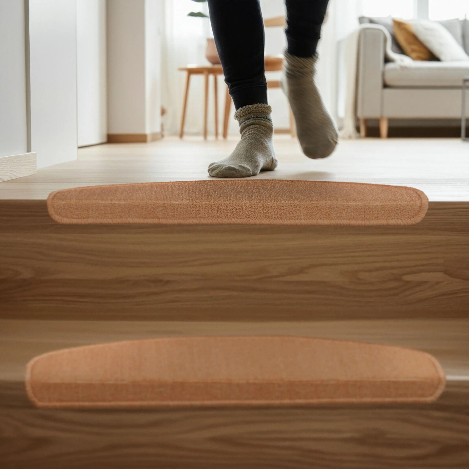 Beige, selbstklebende Treppenmatten auf Holzstufen. Eine Person nutzt die rutschhemmenden Stufenmatten für Komfort & Sicherheit.