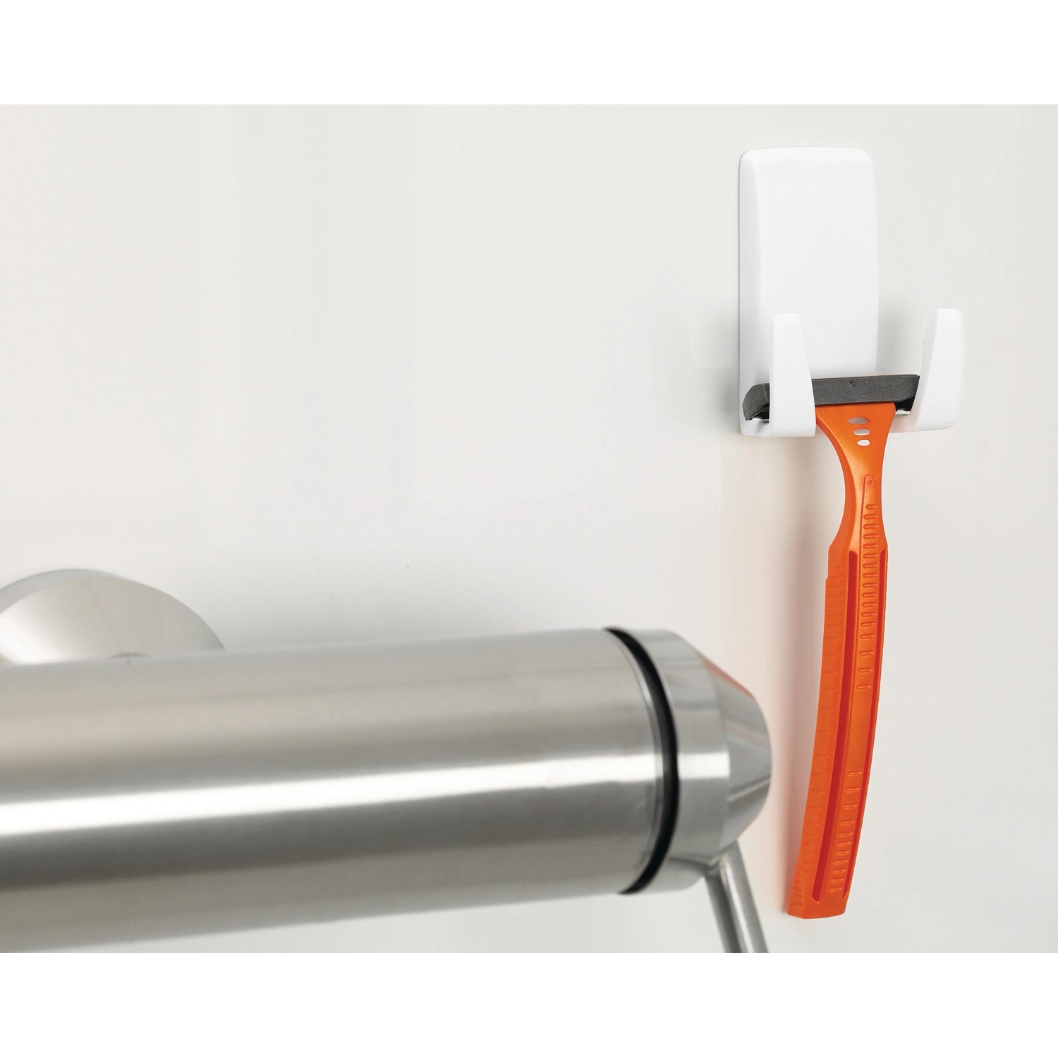 Weißer Tesa Rasiererhalter mit orangefarbenem Rasierer an Badezimmerwand.