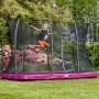 Mädchen springt auf pinkfarbenem Salta Bodentrampolin Comfort Edition mit Sicherheitsnetz im Garten.