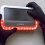 Bosch Smart Home Außensirene mit rotem Blinklicht wird von Händen in schwarzen Handschuhen manipuliert.
