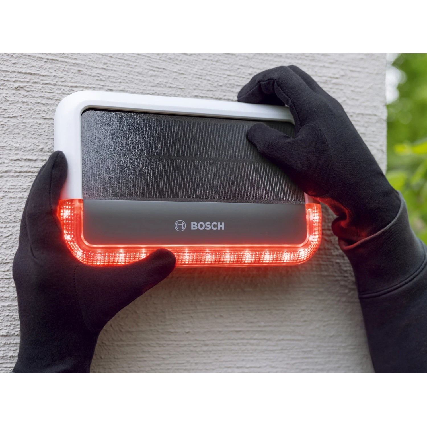 Bosch Smart Home Außensirene mit rotem Blinklicht wird von Händen in schwarzen Handschuhen manipuliert.
