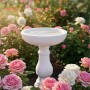 Weiße Relaxdays Vogeltränke aus Polyresin auf Säule, antik, mit Wasser, umgeben von Rosen im Garten.