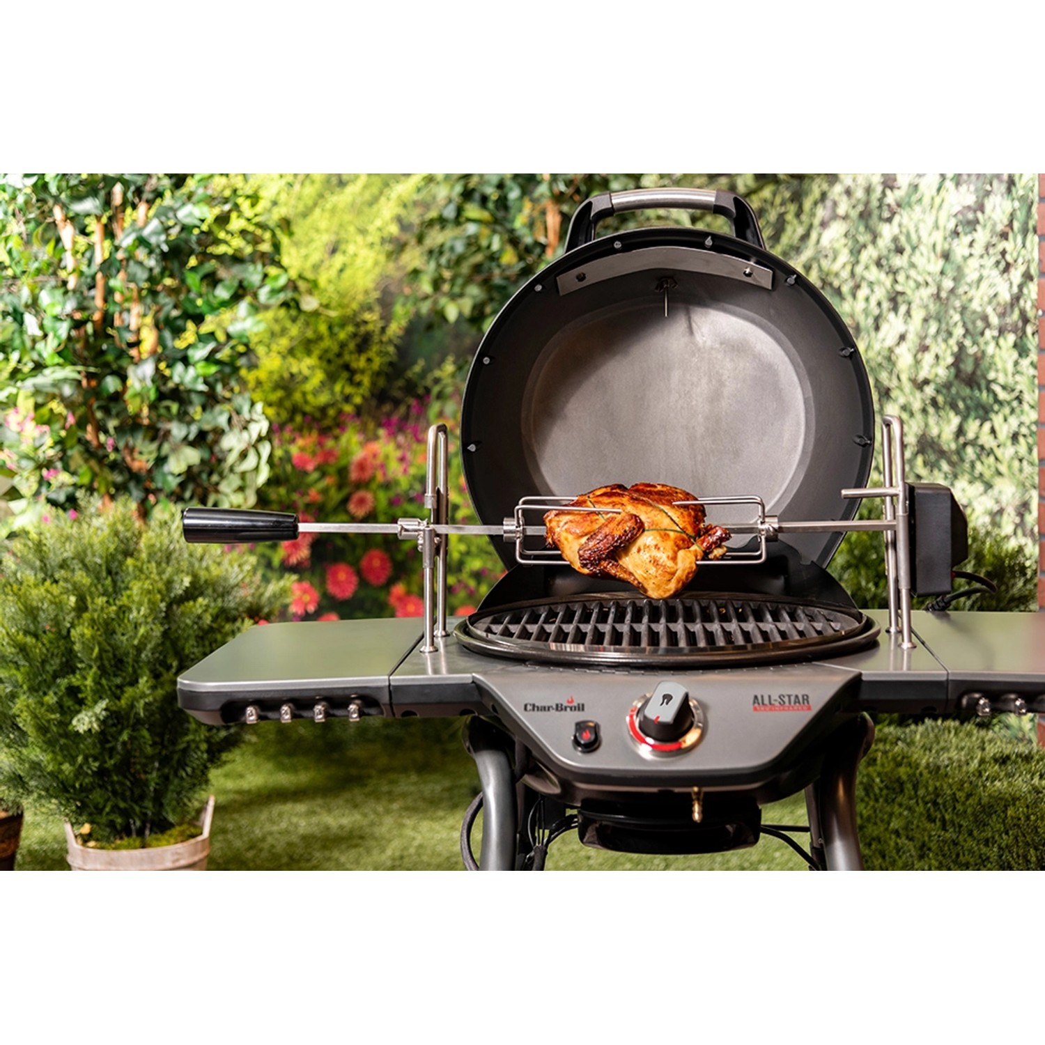 Char-Broil All-Star Grill mit Grillspieß und Brathähnchen im Garten.