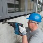 Handwerker bohrt mit blauem Bosch Professional Akku-Bohrhammer GBH 18V-26 in Betonwand. Kabelloses Schlagbohren für Bau.