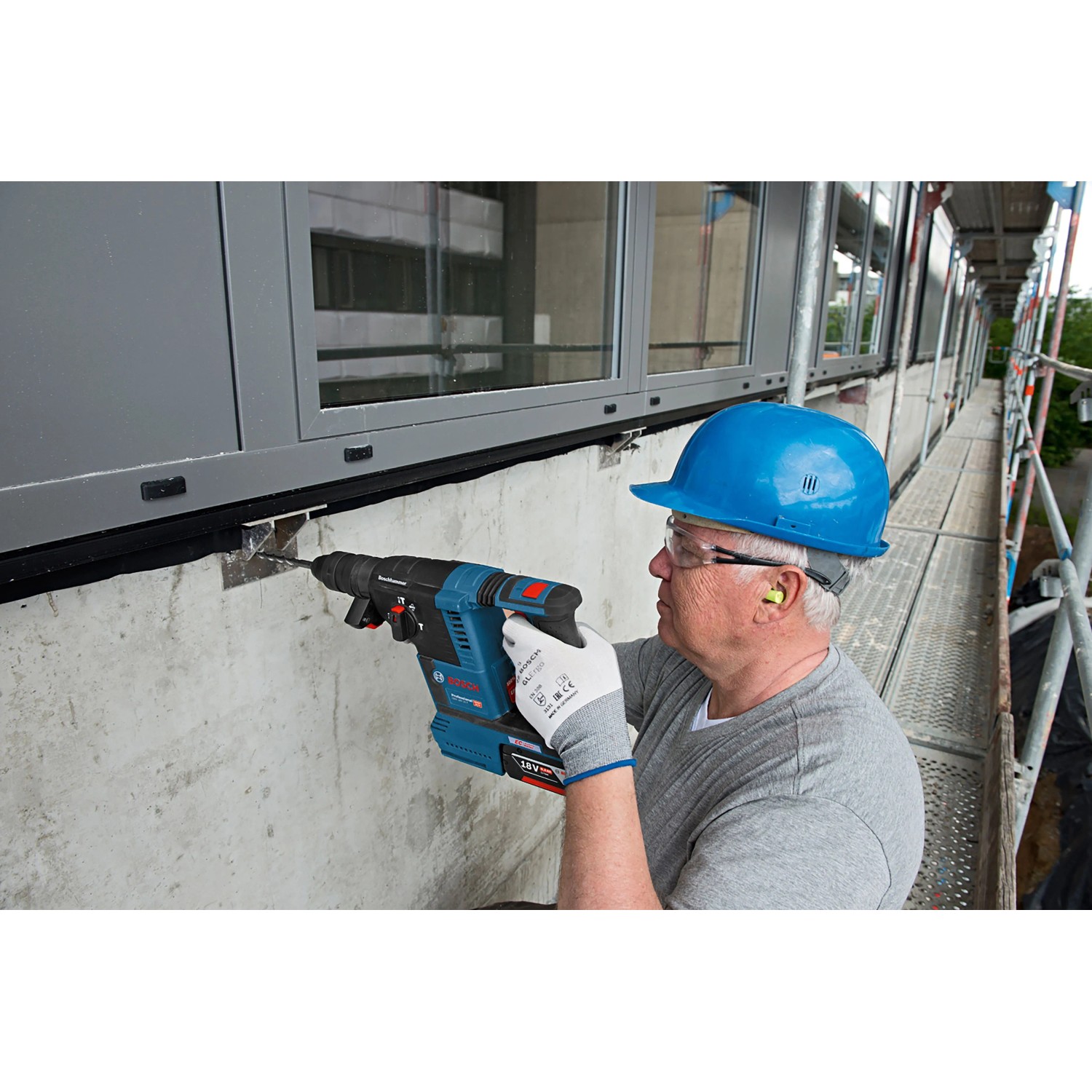 Handwerker bohrt mit blauem Bosch Professional Akku-Bohrhammer GBH 18V-26 in Betonwand. Kabelloses Schlagbohren für Bau.