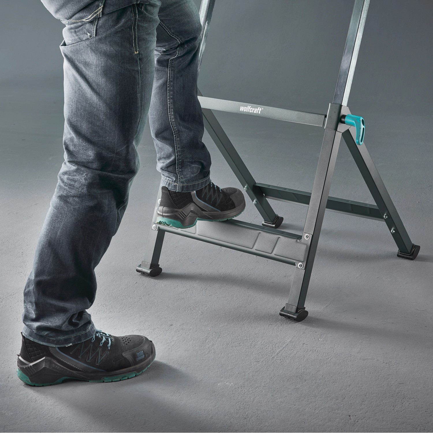 Person steigt auf Wolfcraft Master 650 Ergo Werkbank. Höhenverstellbarer Arbeitstisch.