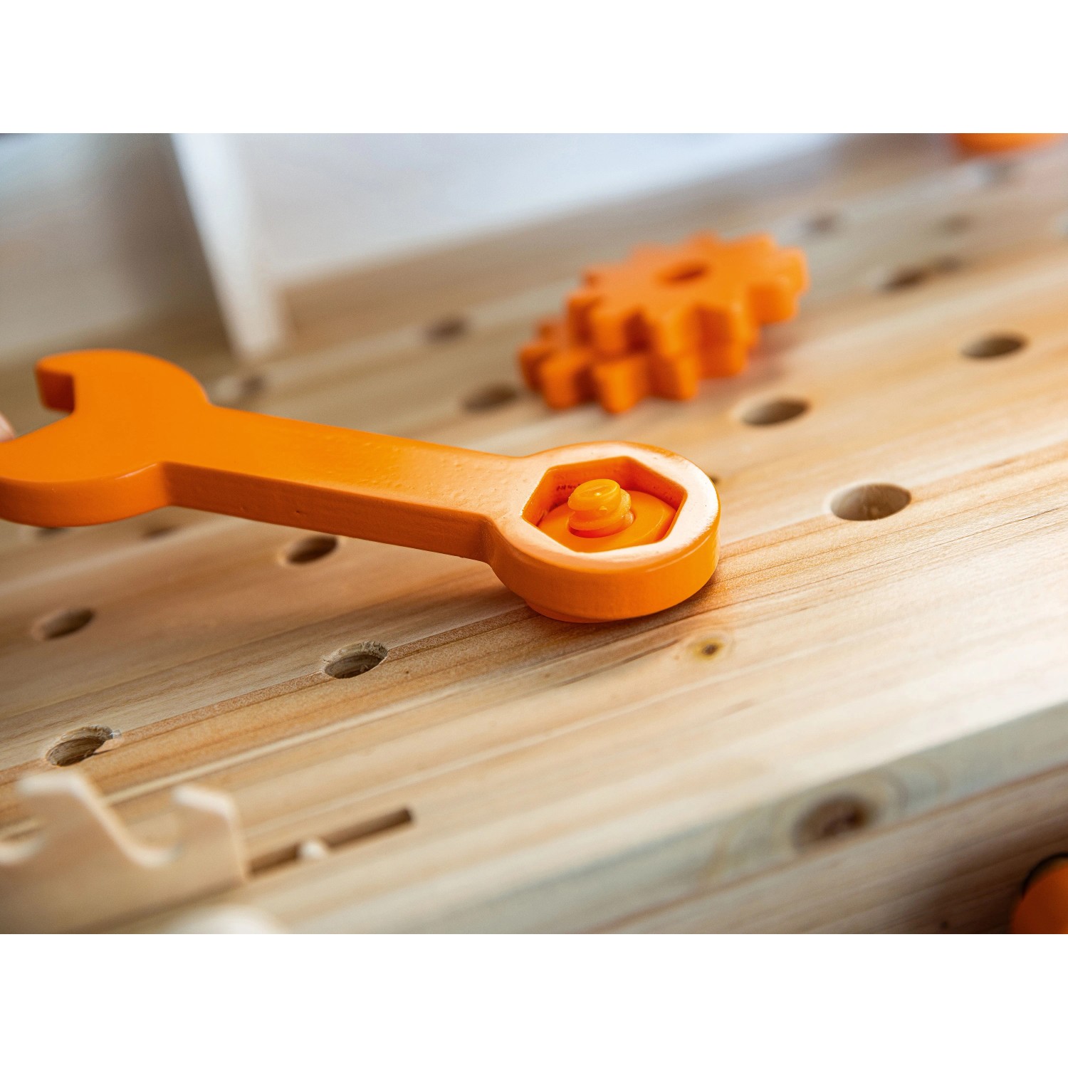 Orangefarbener Spielzeug-Schraubenschlüssel auf OBI Kinderwerkbank aus Holz, Schraube und Zahnräder.