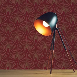 Rote Tadessi Vliestapete mit goldenem Art Deco Grafikmuster. Eine schwarze Stehlampe steht auf einem Holztisch davor.