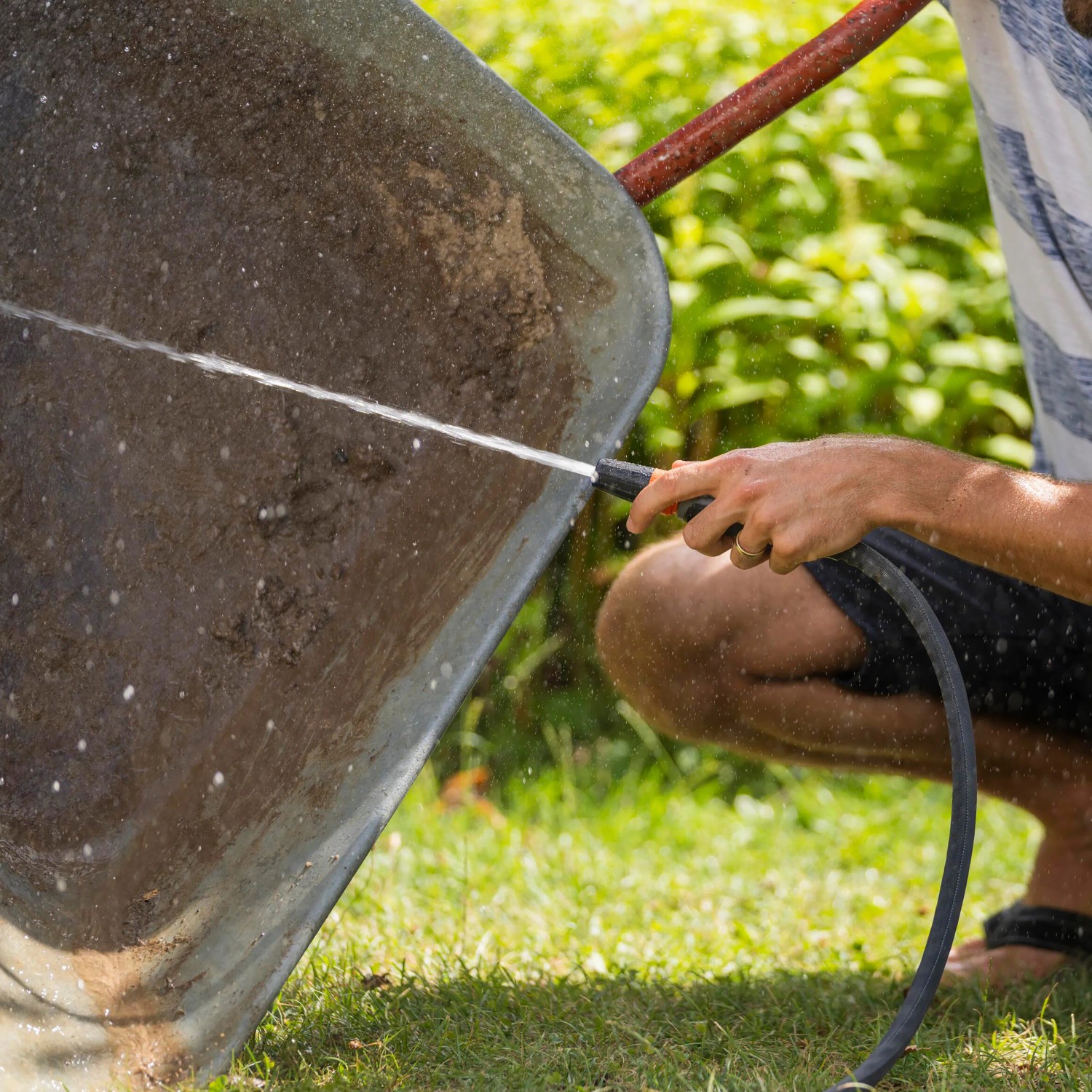 Gartenschlauch-Set Liano™ Life von Gardena im Einsatz: Eine Person reinigt eine Schubkarre mit dem Wasserschlauch.