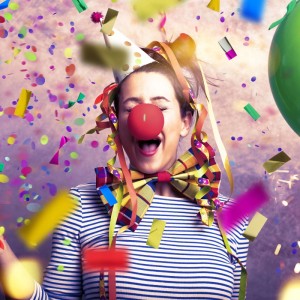 Lachende Person mit Partyhut und roter Nase im bunten Konfettiregen. Party-Popper für Feiern & Events.