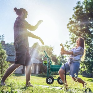 Grüner Relaxdays Gartenschlauchwagen aus Metall mit Kurbel und 4 Rädern im Einsatz. Paar bewässert Garten.