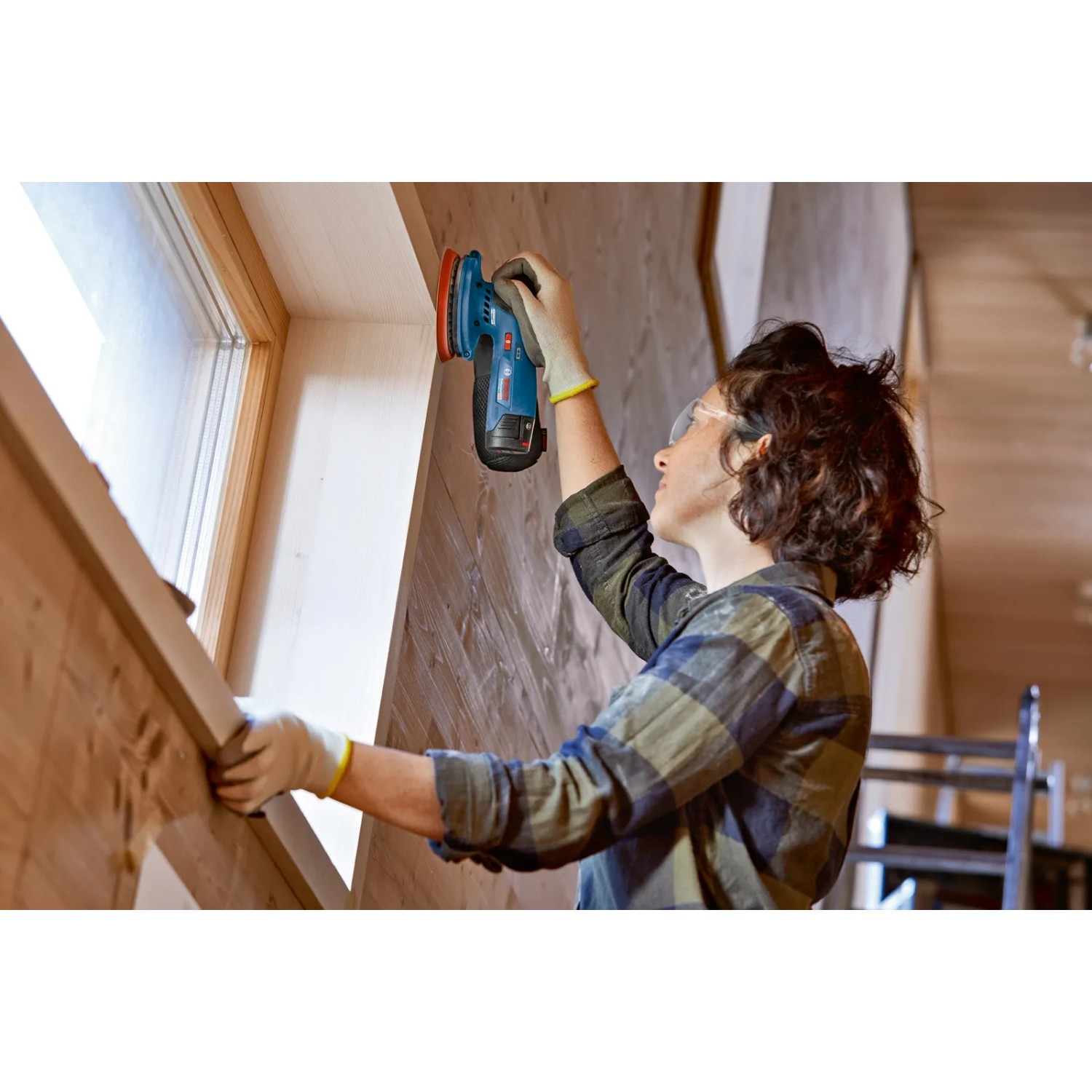 Frau schleift Holz mit Bosch Professional Akku-Exzenterschleifer GEX 12V-125. Schleifmaschine mit Staubbeutel.