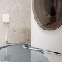 Shelly Wassersensor Flood Gen4 in Weiß mit Kabel, der ein Wasserleck neben einer Waschmaschine detektiert.