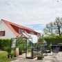 Schwarzes Halls Gewächshaus Qube+ 816 mit 13 m² im Garten, umgeben von Pflanzen.
