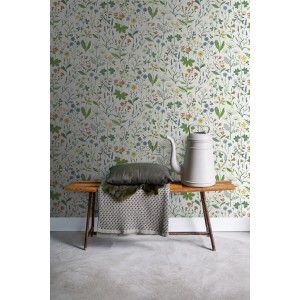 ESTAhome Vliestapete Feldblumen Multicolor auf Wand hinter Bank mit Kissen und Gießkanne.