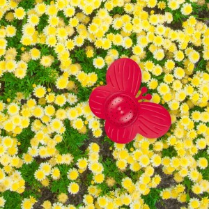 Roter Schmetterling-Gartensprinkler in gelbem Blumenbeet. Dekorativer Regner für Garten, Rasen und Abkühlung.