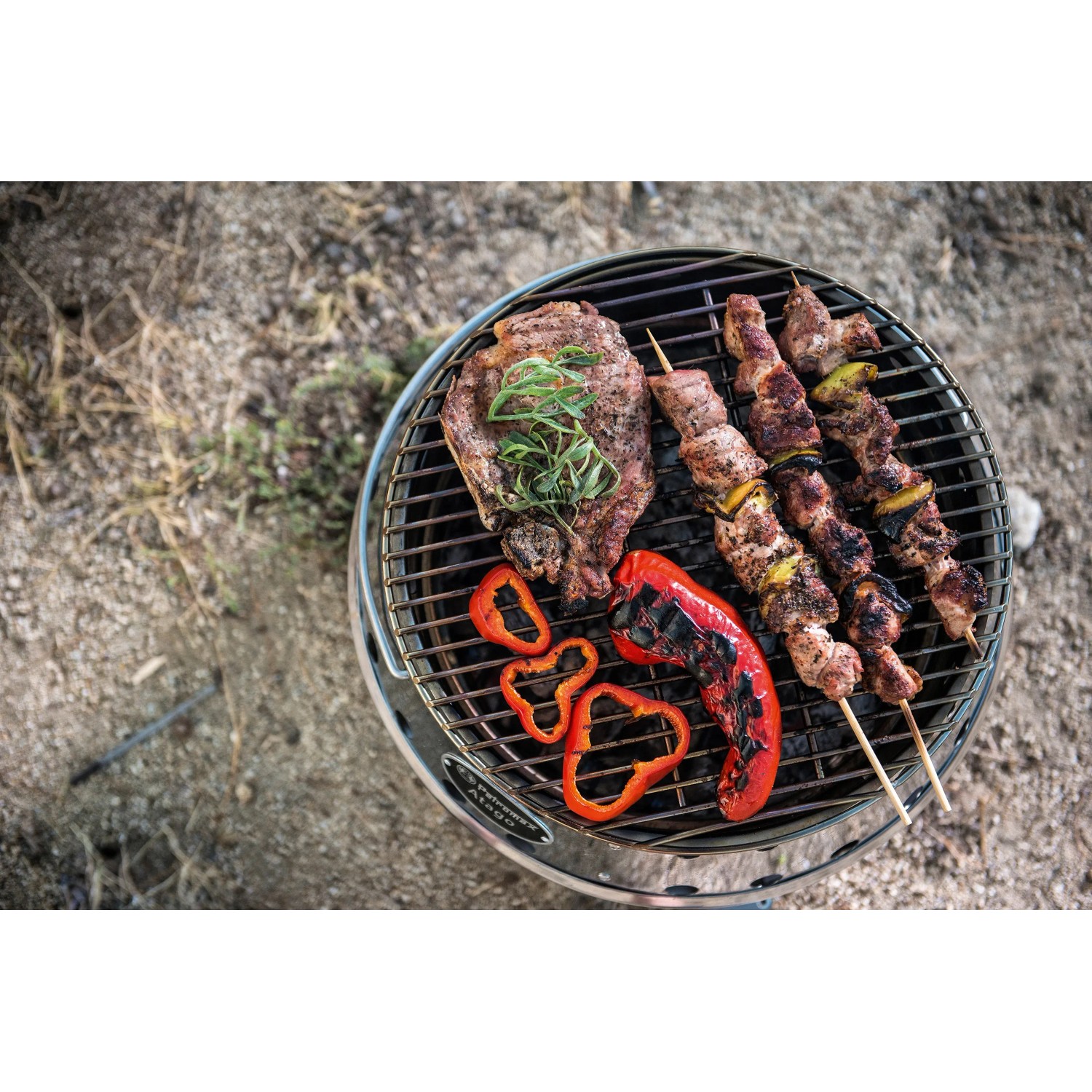 Petromax Atago Grill-Set mit Steak, Spießen und Paprika auf dem Grillrost.