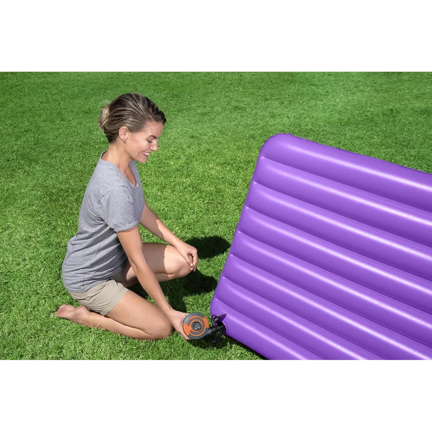 Frau pumpt lila Luftmatratze mit Sidewinder™ 12-V-Elektro-Luftpumpe auf Rasen auf.