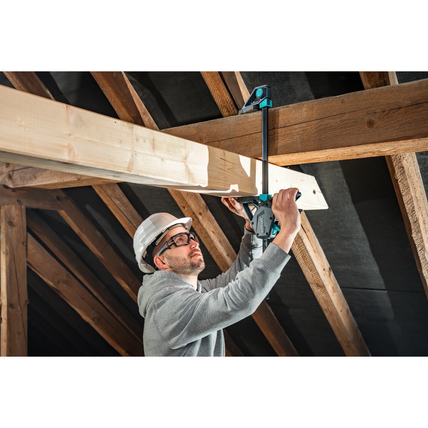 Handwerker mit Wolfcraft Einhandzwinge Pro Max 150 mm beim Spannen eines Holzbalkens.