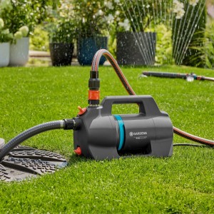 Gardena Gartenpumpe 5400 Silent im Einsatz: Graue Pumpe mit Schläuchen auf Rasen unter fallendem Wasser.