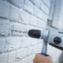 LUX Steinbohrer bohrt Loch in weiße Ziegelwand mit Schlagbohrmaschine.