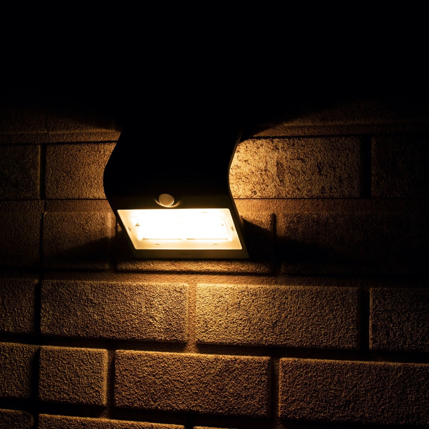 Schwarze LED Solar-Außenleuchte mit Sensor an einer Backsteinwand. Flutlicht mit 400 Lumen.