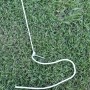 Detailaufnahme von Haken und Seil zur Befestigung der Leco Zeltplane auf Rasen.