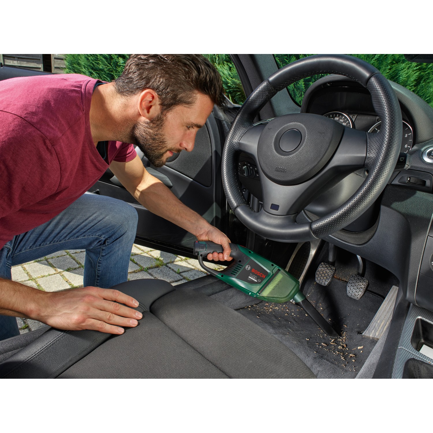 Mann reinigt Auto mit Bosch Akku-Handstaubsauger EasyVac 12. Kompakter Handstaubsauger in Grün.