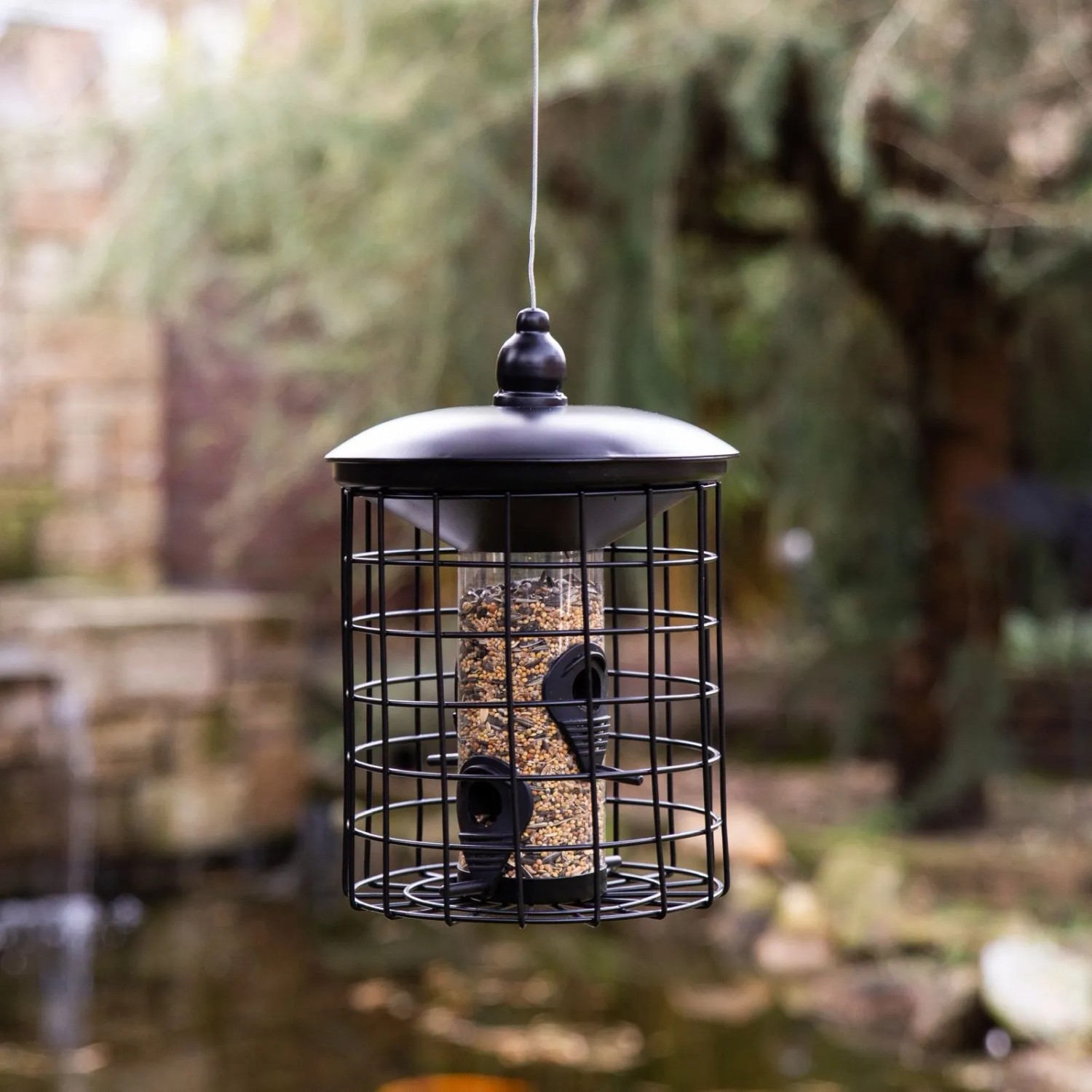 Schwarzes CULT at home Vogelfutterhaus aus Metall mit Futter, hängend im Garten. Ideal für Wildvögel.