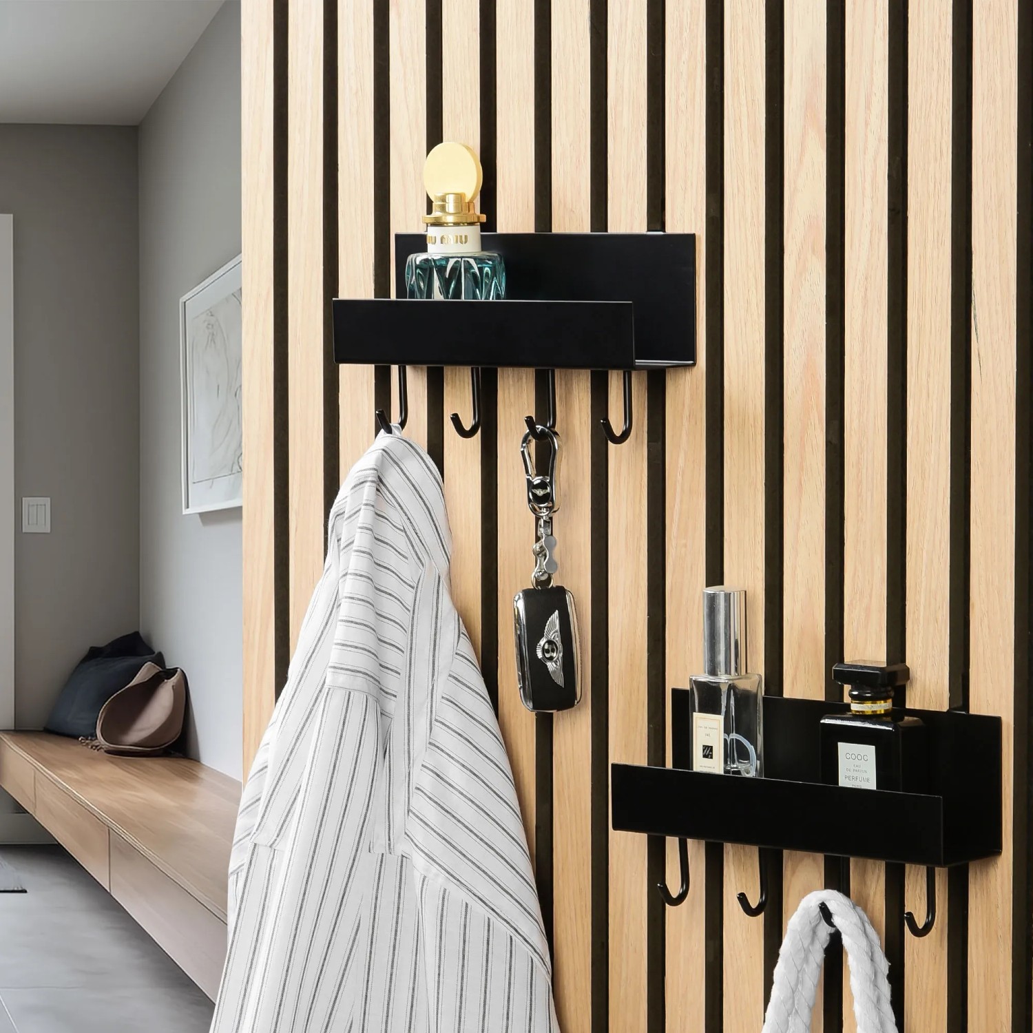 Schwarzes DenPanels Regal mit 4 Stiften an Akustikpaneel mit Jacke, Schlüssel und Deko.