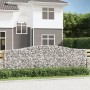Gabionen-Hochbeet mit Bogen, gefüllt mit Steinen, als dekorative Gartenmauer vor einem Haus.