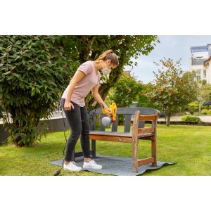 Frau sprüht Holzbank mit Wagner Farbsprühsystem W 125 im Garten.