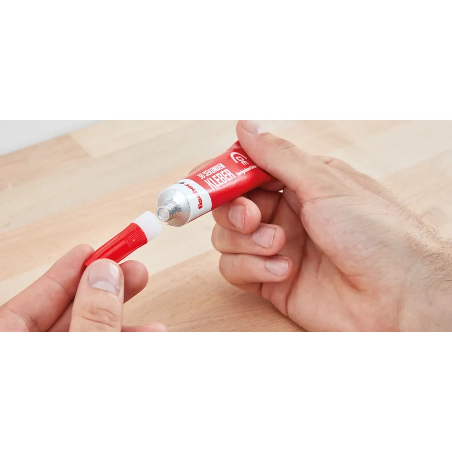 Hände öffnen rote Tube Fischer 30 Sekunden Kleber 15g. Sekundenkleber und Verschluss sind zu sehen.