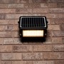 Schwarze LED Solar-Außenleuchte mit Sensor an einer Backsteinwand. Flutlicht mit 10W Leistung.