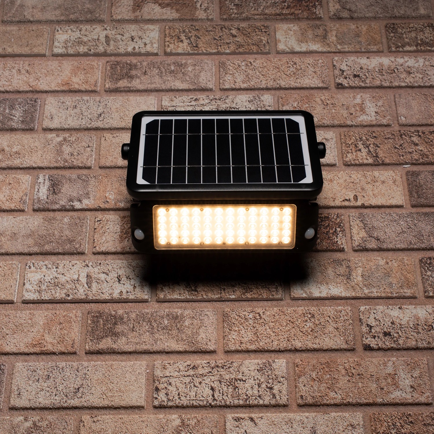 Schwarze LED Solar-Außenleuchte mit Sensor an einer Backsteinwand. Flutlicht mit 10W Leistung.