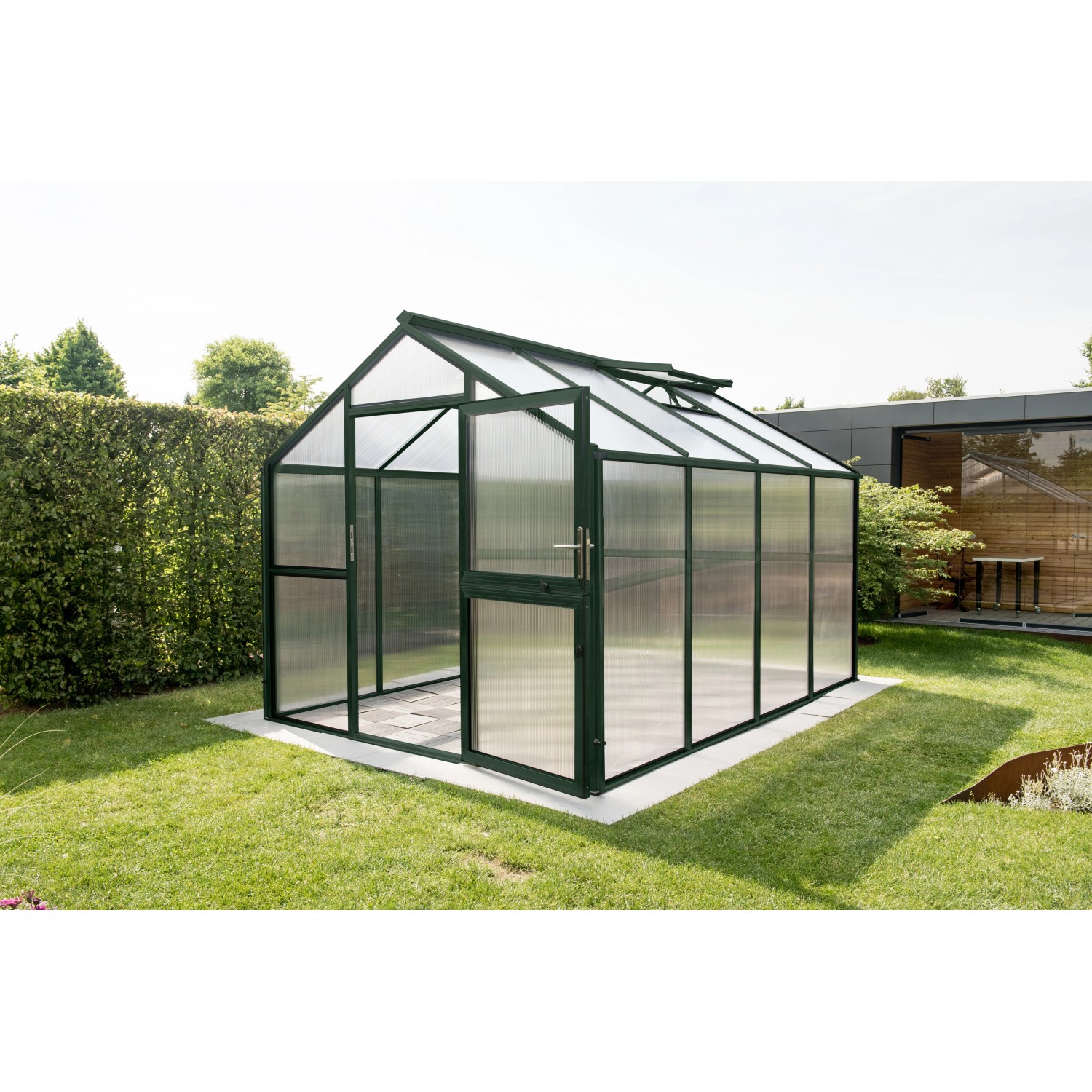 KGT Gewächshaus Novum IV, tannengrün, 11,14 m², mit geöffneter Tür im Garten.