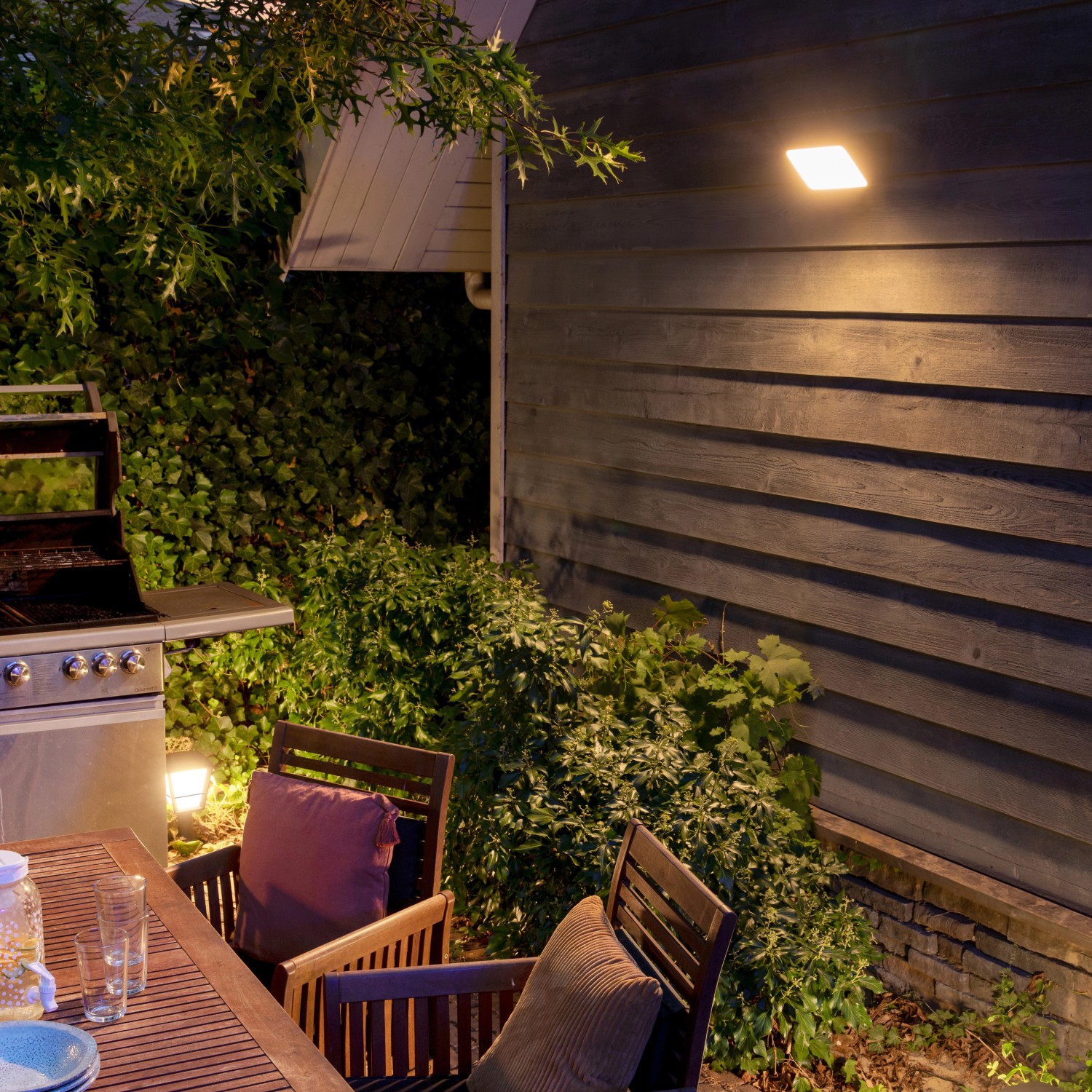 Philips Hue Discover LED-Wandleuchte beleuchtet Terrasse mit Grill und Sitzgruppe.